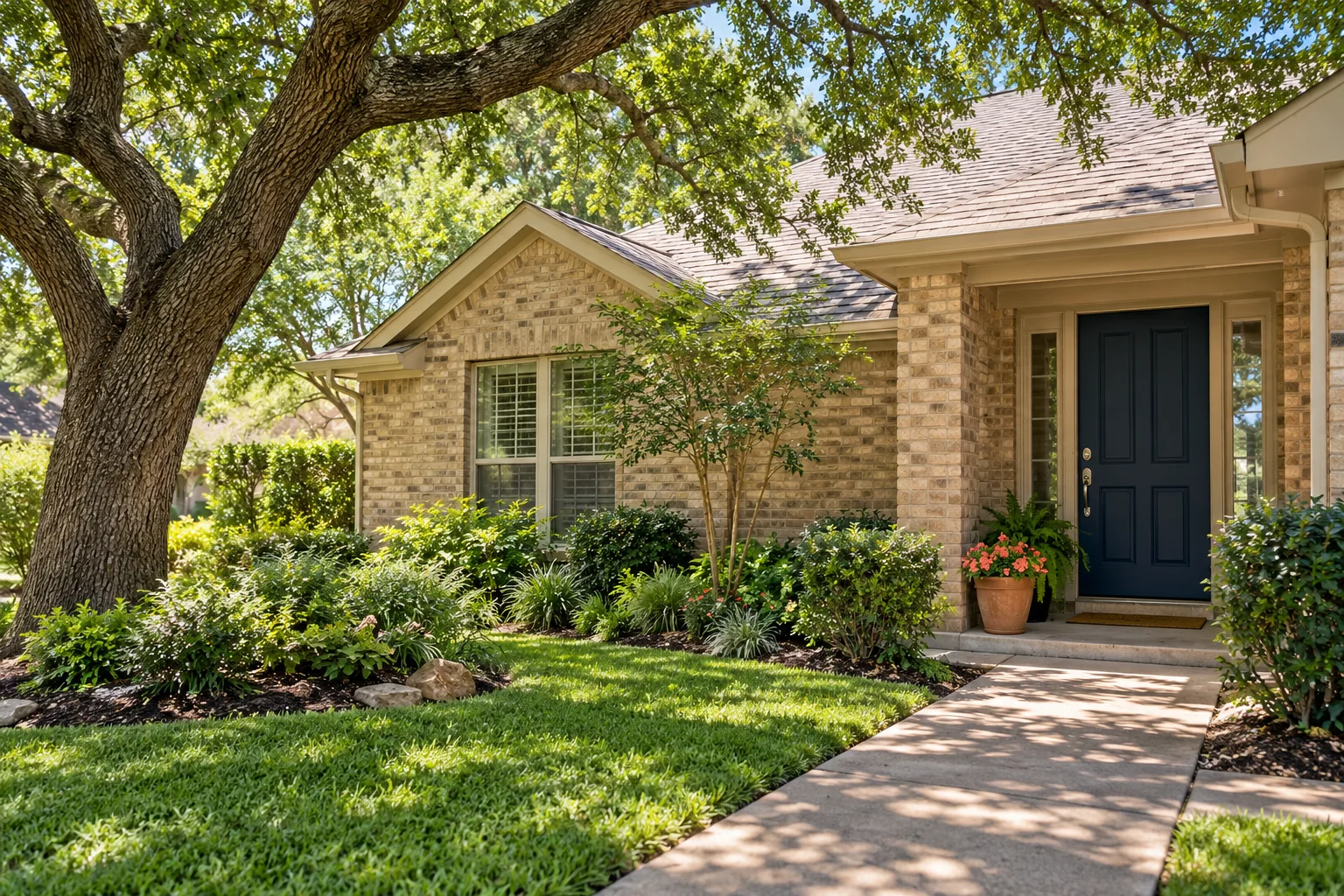 A brick home shaded by a leafy oak, with a blue front door